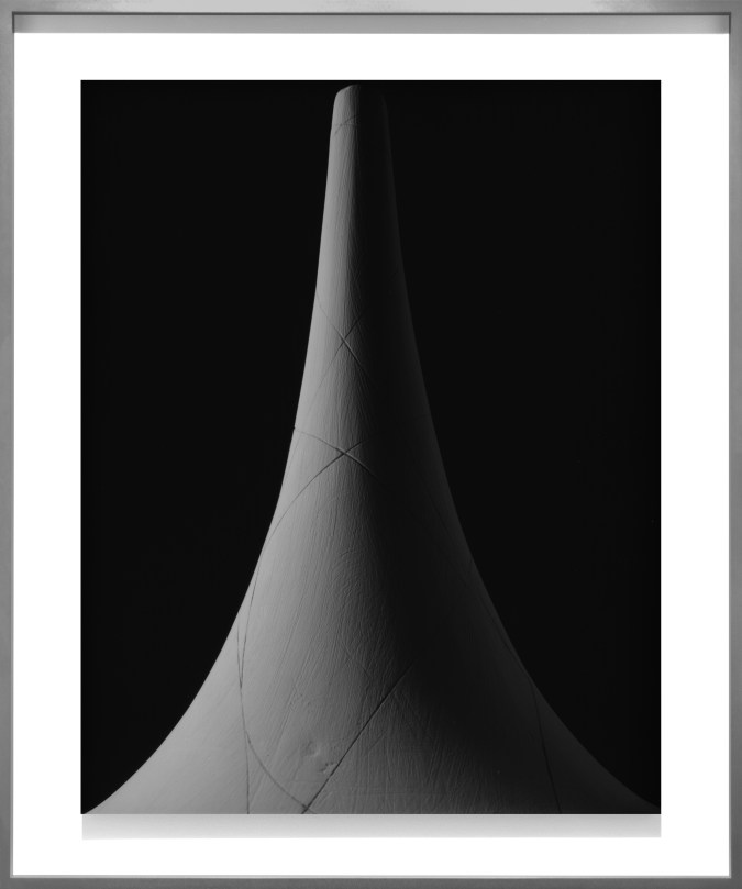Black and white photograph of a cone shaped form against a black background framed in metal