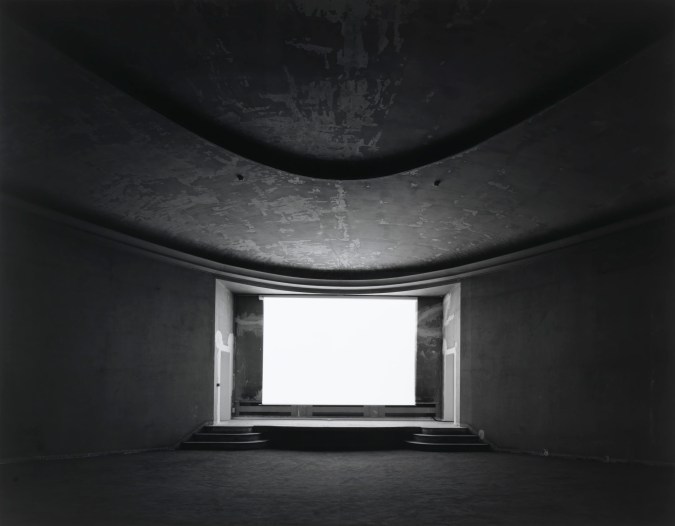 Black-and-white photograph of an empty theater with a glowing blank white screen