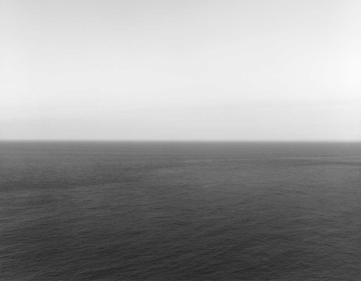 Black-and-white photograph of a rippled seascape with a bright white sky and dark gray sea