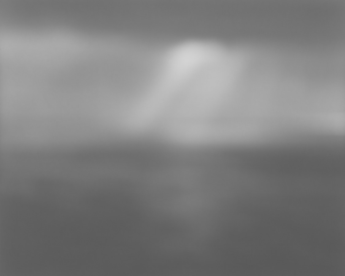 Black-and-white photograph of a very foggy seascape, with a ray of light in the center of the sky