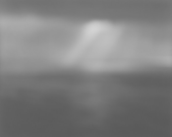 Black-and-white photograph of a very foggy seascape, with a ray of light in the center of the sky