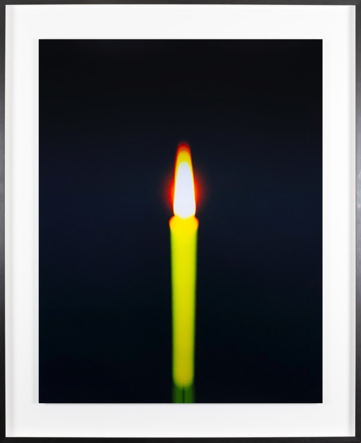 Color photograph of a burning candle with a black background