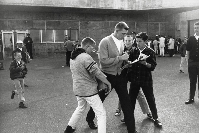 Black-and-white photograph of a group of boys following a young man holding some papers