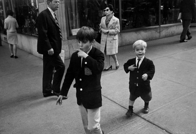 Black-and-white photograph of two boys in school uniforms passing through a street corner
