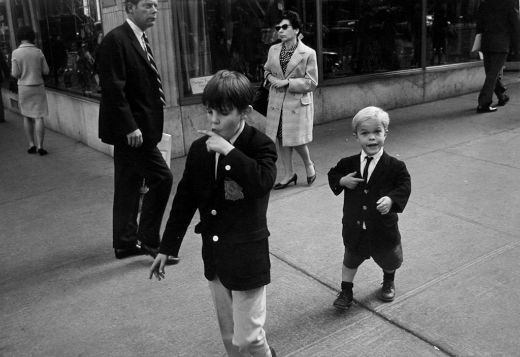 Black-and-white photograph of two boys in school uniforms passing through a street corner